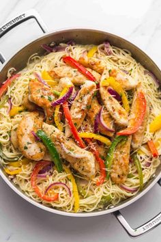 chicken and vegetable pasta in a skillet on a white countertop with tongs