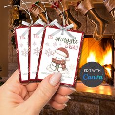 someone holding up three christmas gift tags in front of a fireplace