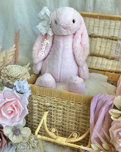 a pink stuffed animal sitting in a basket next to some flowers and other items on a table