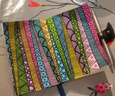 an open notebook with colorful designs on it and a pen laying next to the cover