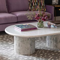 a table with two books on it in front of a purple couch and flower vase