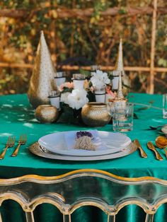 a table set with plates, silverware and gold vases on top of it