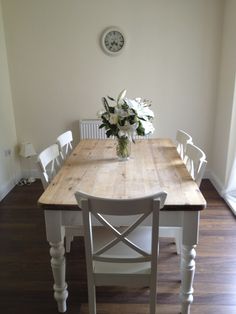 a wooden table with white chairs and flowers in a vase on top of the table