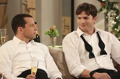 two men sitting on a couch talking to each other with wine glasses in their hands