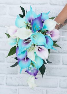 a bridal bouquet with blue and white flowers in front of a brick wall background