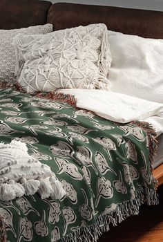 an unmade bed with white and green blankets on top of it next to a brown couch