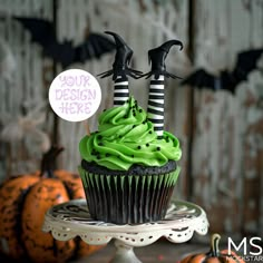 two cupcakes with green frosting and black decorations are on a cake stand