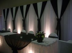 a banquet table with black and white drapes on the wall, lit by candles