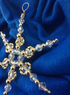 a gold snowflake ornament on a blue cloth with some beads hanging from it