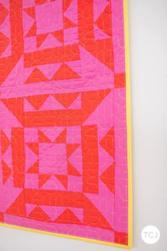 a red and pink quilt hanging on the wall next to a white wall with yellow trim