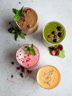 three smoothies are lined up on a table with mints and berries in them