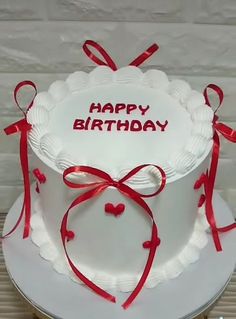 a white birthday cake with red ribbon and happy birthday written on the top, sitting on a table