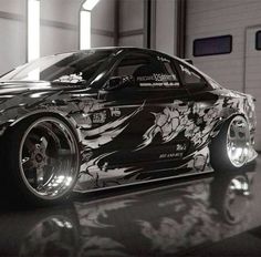 a black and white photo of a car with floral designs on the hood, parked in a garage