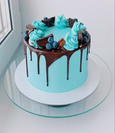 a cake with blue frosting and chocolate icing on a plate next to a window