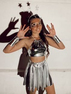 a woman dressed in silver is posing for the camera with her hands up and arms outstretched