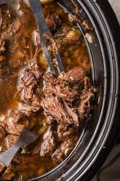 a slow cooker filled with shredded meat and gravy next to a spoon