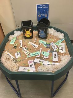 a green table topped with lots of writing on top of paper and plastic cups filled with magnets