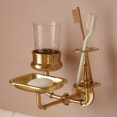 two toothbrushes and a cup on a gold plated wall mounted holder for toothpaste