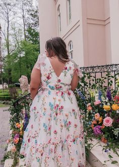 a woman in a white floral dress standing on the steps next to some colorful flowers