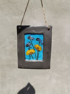 a metal frame with yellow flowers hanging from it's side and a shadow on the wall behind it