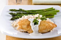 a white plate topped with chicken and asparagus covered in ranch dressing next to rice