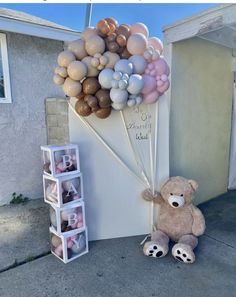 a teddy bear sitting next to a bunch of balloons on the side of a building