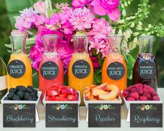 an assortment of juices and fruit in containers on a table with flowers behind them