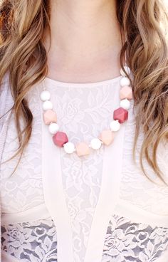 a woman wearing a white top and pink necklace with red, white and grey beads