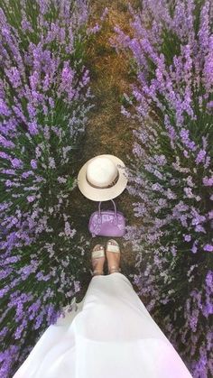 a person wearing sandals and a hat standing in front of purple flowers with their legs crossed