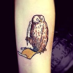 an owl tattoo on the arm with a piece of paper in front of it's leg