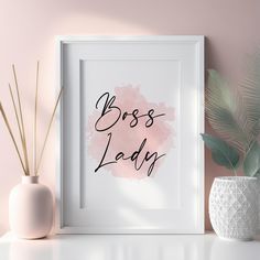 a white vase and some plants on a shelf next to a framed print that says boss lady