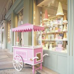 a pink and white ice cream cart sitting in front of a store filled with cakes