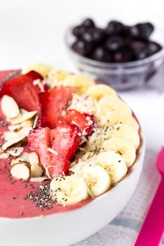 a white bowl filled with fruit and nuts on top of a table next to a pink spoon