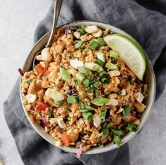 a bowl filled with rice and vegetables on top of a gray cloth next to a spoon