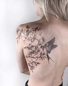 the back of a woman's shoulder with flowers and a bird tattoo on it