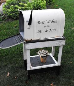 a white mailbox sitting on top of a wooden stand with flowers in the bottom