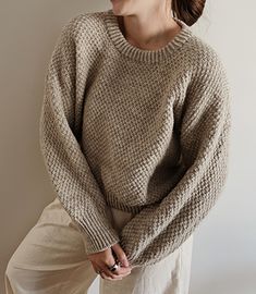 a woman is wearing a brown sweater and white pants