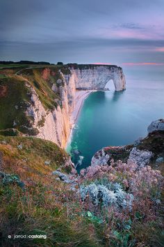 an image of the cliffs and water at sunset with a bridge in the distance,