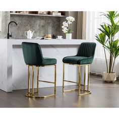 two green velvet bar stools in front of a white marble countertop with potted plants