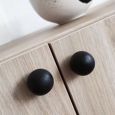 two black knobs on the side of a wooden cabinet next to a white vase