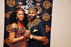 a man and woman standing next to each other in front of a wall with an african design on it