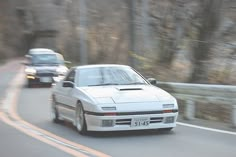 two cars driving down the road in front of each other on a highway with trees behind them