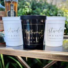 three white and black cups sitting on top of a wooden table next to each other