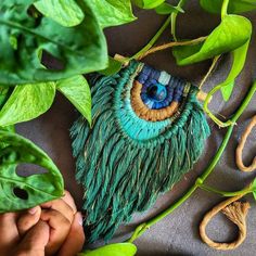 a person holding a plant with green leaves around it and an eye made out of yarn