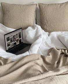 an open laptop computer sitting on top of a bed covered in white sheets and blankets