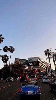 cars are driving down the street in front of tall buildings and palm trees on a sunny day