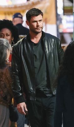 a man in a black leather jacket walking down the street with other people behind him