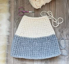 a crocheted skirt next to a ball of yarn, scissors and knitting needles