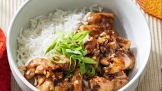 a white bowl filled with rice and meat on top of a wooden table next to an orange napkin