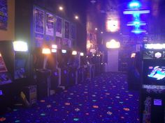 a row of arcade machines in a room with blue carpet and neon lights on the walls